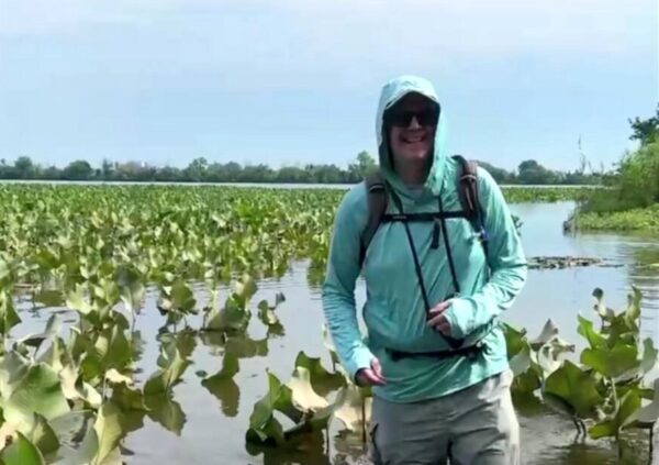 Jeremy wearing a sun-protective hooded shirt standing in shallow water surrounded by water lilies.