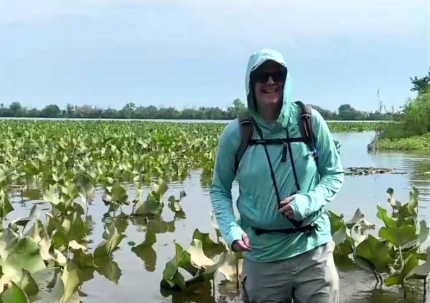 Jeremy wearing a sun-protective hooded shirt standing in shallow water surrounded by water lilies.