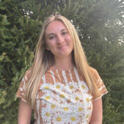 A young woman wearing a shirt with daisies on it smiles for the camera.